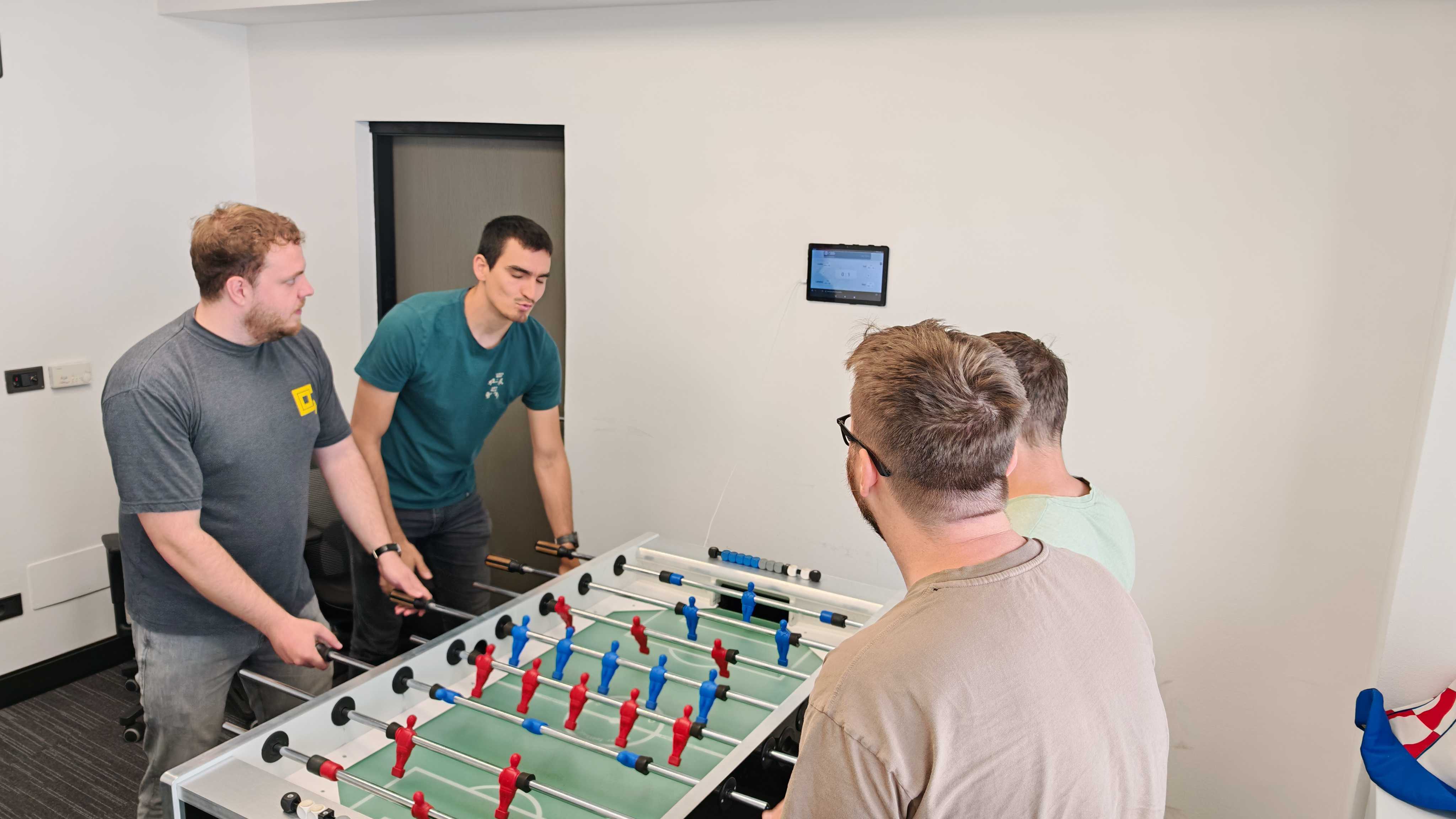 Image depicts 4 people playing a foosball match.
